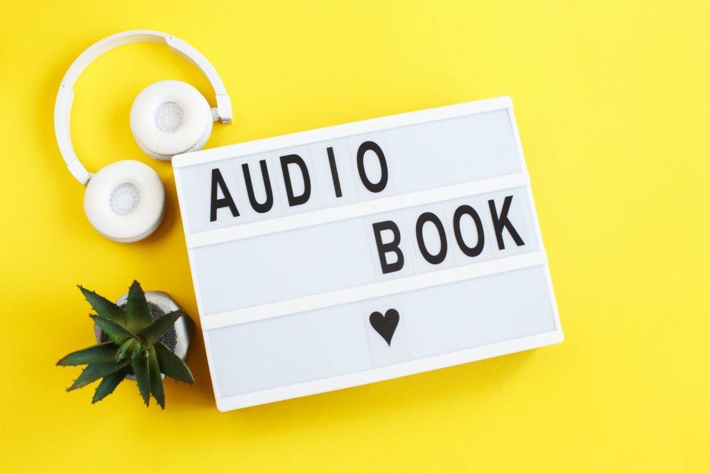 inscription audiobook on a light box with modern white headphones on a yellow background