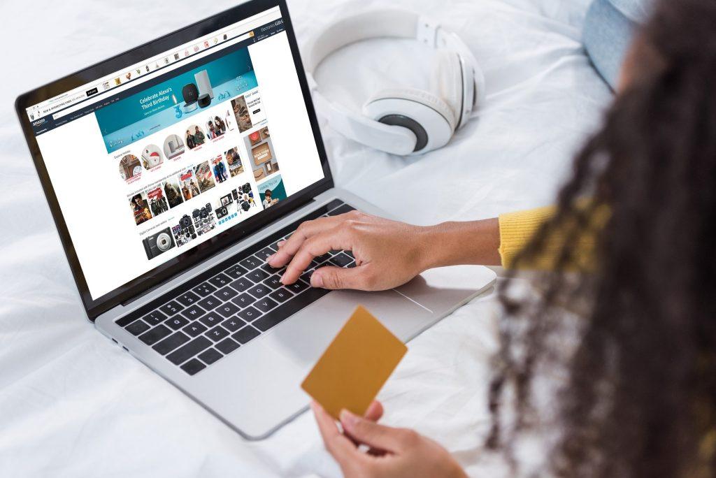 cropped image of woman holding credit card and using laptop with amazon on screen